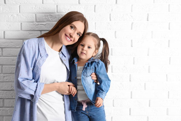 Young mother and little daughter near white brick wall. Space for text - Foto, imagen