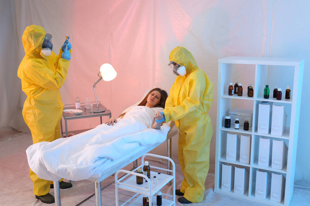 Paramedics wearing protective suits examining patient with virus in quarantine ward - Photo, image