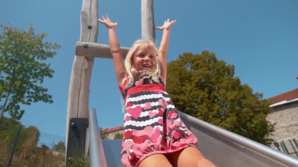 SLOW MOTION: Fröhliches kleines Mädchen spielt auf Spielplatz und rutscht die Rutsche hinunter - Filmmaterial, Video