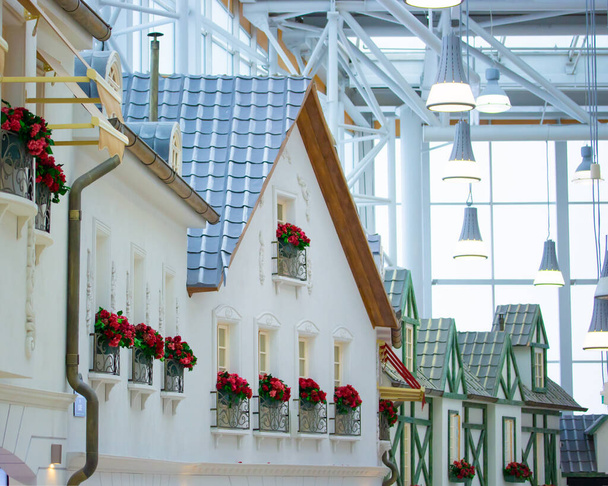 La décoration du centre est un centre commercial, une maison blanche dans le style européen avec des fleurs rouges sur les fenêtres avec une clôture métallique. Belle maison minimaliste avec toit carrelé et poutres en bois
. - Photo, image