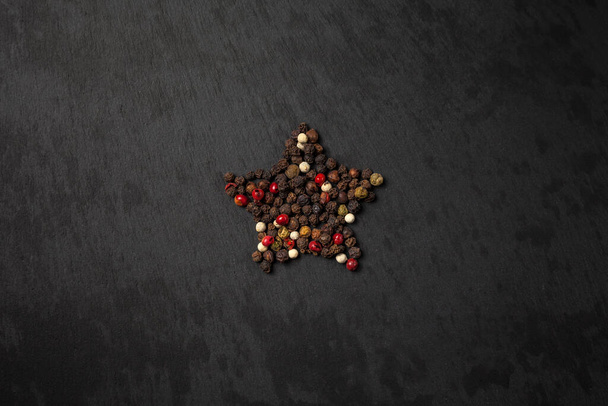 Pimienta de pimienta sobre un fondo negro, dispuesta en forma de estrella. Pimientos rojos, blancos, verdes y negros. guisantes pimienta. fondo de pizarra negro
 - Foto, Imagen