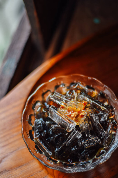 Grass jelly in syrup with ice cubes leaf jelly in bowl on wood table, Thai dessert grass jelly, Chao Koui - Foto, imagen