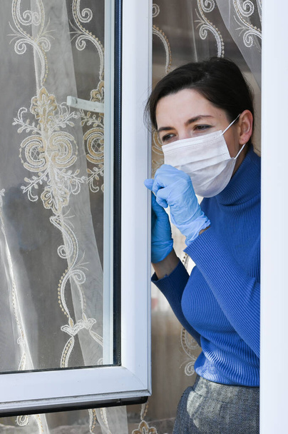 дівчина в карантині з маскою дивиться у вікно вдома - інфекція і поширення нового коронавірусу 2019 року. Дівчина-підліток дивиться через вікно з маскою
 - Фото, зображення
