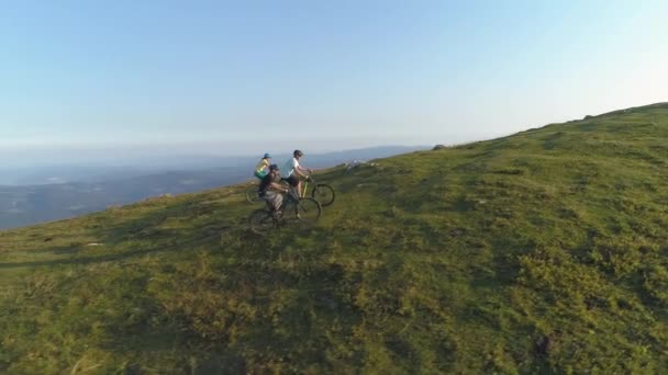 AERIAL: Friends pedalling electric bikes up a grassy hill on a sunny afternoon. - Footage, Video