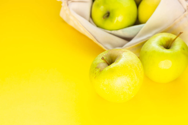 Reusable cotton textile bag with green apples on a yellow paper background. The concept of zero waste, ecology shopping.  - Foto, Imagen