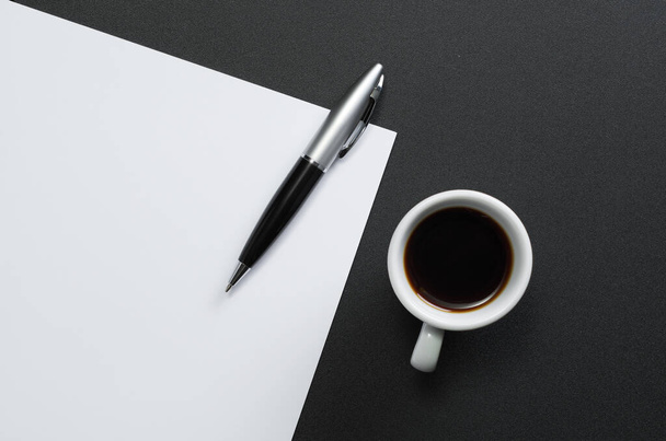 Sábanas de papel blanco vacío con un bolígrafo y una taza de café en una mesa negra, vista superior
 - Foto, imagen