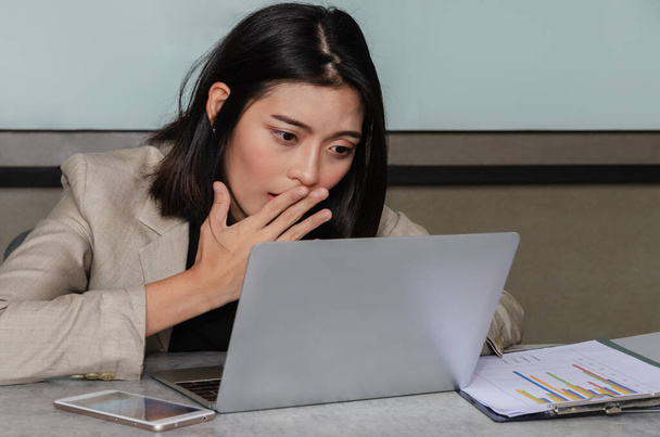 Zaskoczona azjatycka bizneswoman używająca laptopa w pokoju konferencyjnym, zakrywająca usta z uprzejmości. Koncepcja biznesu i biura. - Zdjęcie, obraz