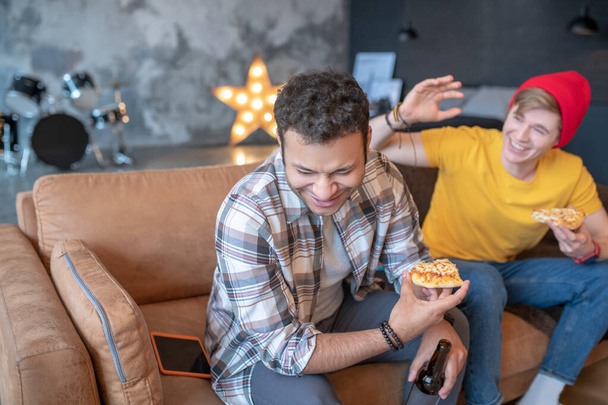 Two young men sitting on the sofa and eating pizza - Photo, Image