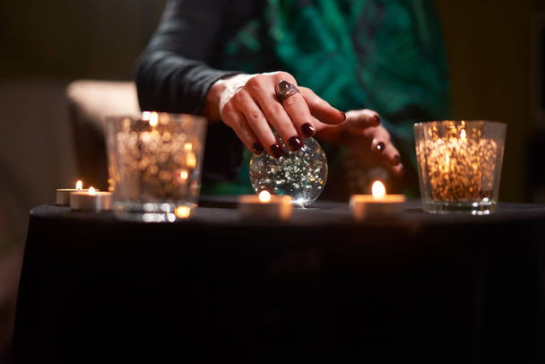 Close-up of fortuneteller woman divining on magic ball at table with burning candles - Foto, Imagen