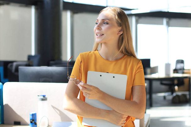 Attractive business woman in smart casual wear looking away and smiling while standing in the office. - Fotoğraf, Görsel