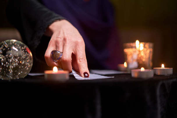 Close-up of fortune teller woman divining on cards sitting at table with burning candles, magic ball - Fotó, kép