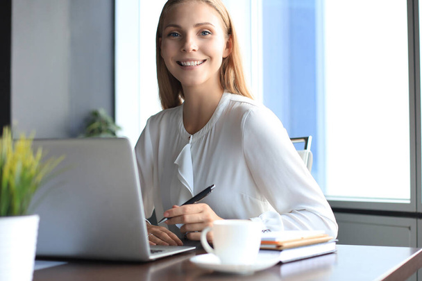 Beautiful smiling business woman is sitting in the office and looking at camera. - 写真・画像