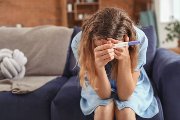 Sad young woman with pregnancy test at home - Foto, Bild