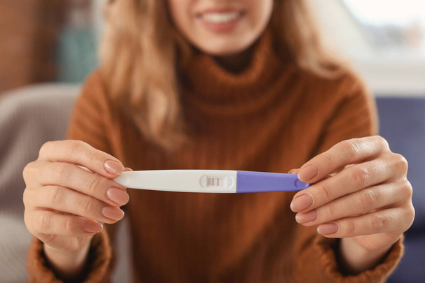 Happy young woman with pregnancy test at home, closeup - Photo, Image