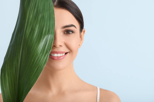 Beautiful young woman with tropical leaf on color background - Φωτογραφία, εικόνα