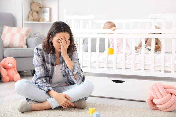 Young woman suffering from postnatal depression near bed with baby at home - Φωτογραφία, εικόνα