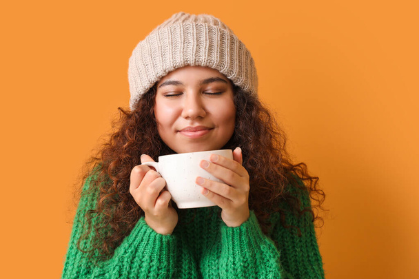 Junge Frau im warmen Pullover und mit einer Tasse heißem Tee auf farbigem Hintergrund - Foto, Bild