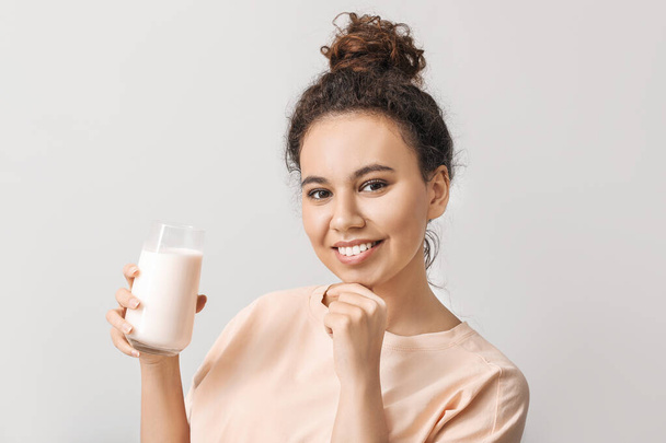 Young African-American woman with milk on light background - Fotó, kép