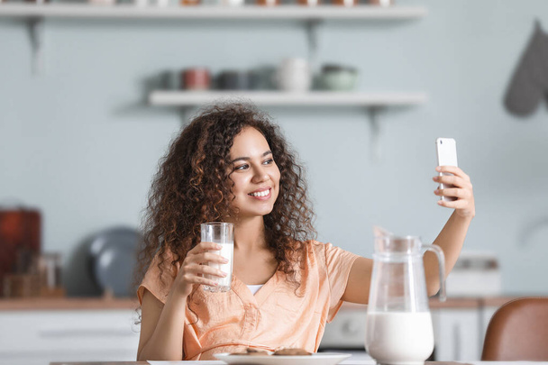 Joven mujer afroamericana con leche tomando selfie en la cocina
 - Foto, imagen