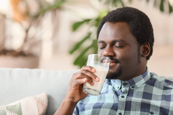 Young African-American man drinking milk at home - 写真・画像