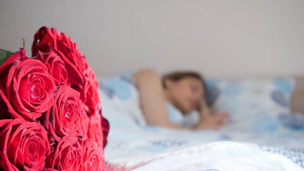 Beautiful woman sleeping in bed. Surprise red rose bouqet waiting for her. Flower delivery. Romantic concept for valentines day, international womens day, engagement and birthday. - Fotoğraf, Görsel