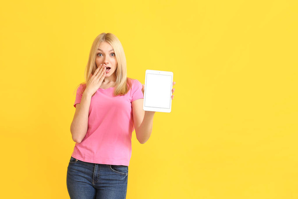 Surprised young woman with tablet computer on color background - Φωτογραφία, εικόνα