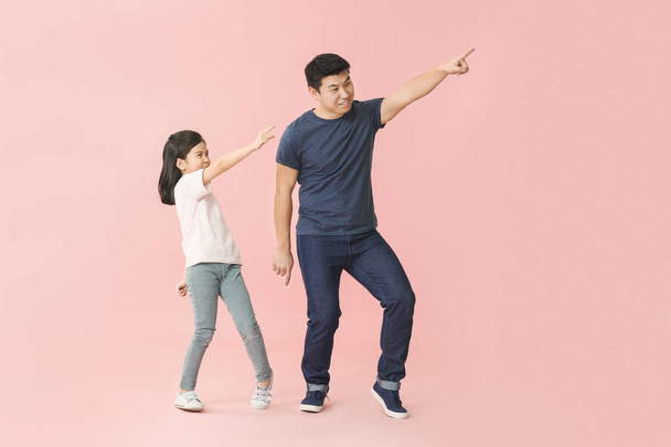 Glücklicher asiatischer Mann und seine kleine Tochter tanzen vor farbigem Hintergrund - Foto, Bild