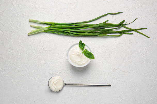 Bol avec crème sure savoureuse, cuillère et oignon vert sur fond blanc
 - Photo, image