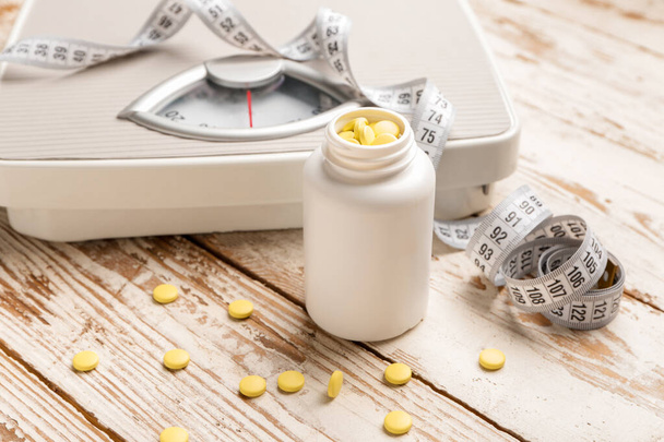Flasche mit Gewichtsverlust-Pillen, Waage und Maßband auf weißem Holzgrund - Foto, Bild