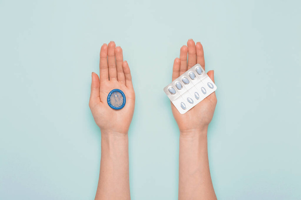 Женские руки с сексуальными таблетками и презервативами на цветном фоне
 - Фото, изображение