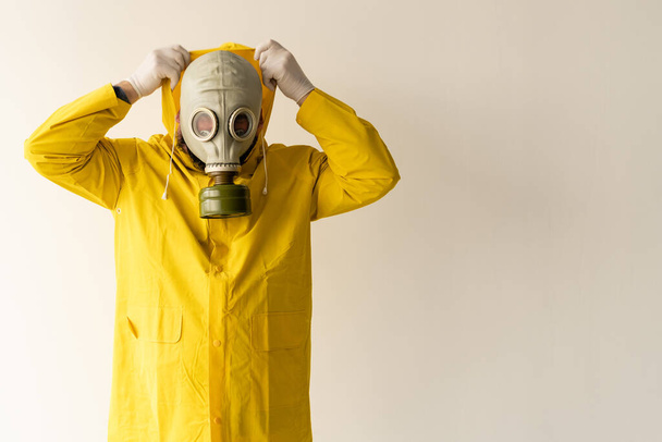 un hombre lleva un traje protector amarillo, se quita o se pone una capucha en la cabeza. máscara de gas en la cara. Protección contra virus y ataques químicos. Lugar para el texto
 - Foto, Imagen