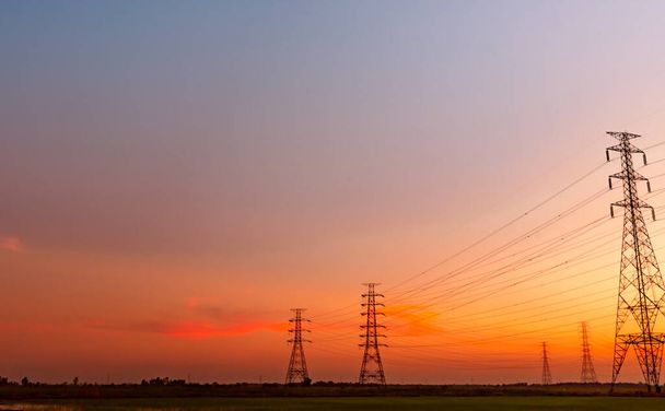 Ηλεκτρικός πυλώνας υψηλής τάσης και ηλεκτρικό καλώδιο με ουρανό ηλιοβασιλέματος. Κάδοι. Ισχύς και ενέργεια. Πύργος δικτύου υψηλής τάσης με καλώδιο καλωδίων. Όμορφο τοπίο με μωβ oad κόκκινο ουρανό. - Φωτογραφία, εικόνα