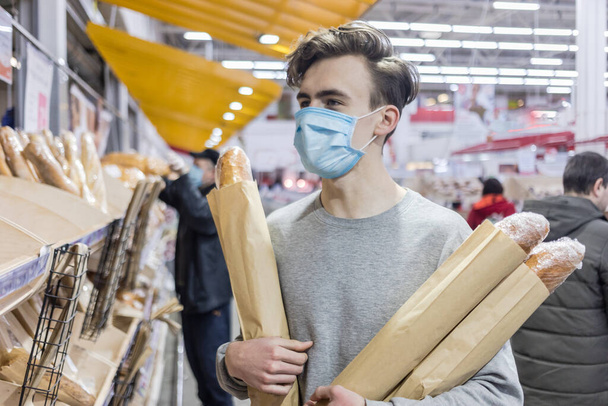 Młody człowiek noszący jednorazową maskę medyczną robi zakupy w supermarkecie podczas epidemii zapalenia płuc. Ochrona i zapobieganie środkom w czasie epidemii. Covid-19 osoba - Zdjęcie, obraz