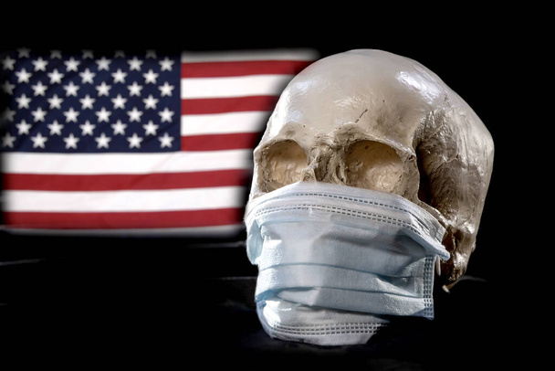 Ludzka czaszka w masce medycznej na tle amerykańskiej flagi. Koncepcja: śmiertelność w Ameryce z powodu koronawirusu, globalnej pandemii, infekcji śmiertelnym wirusem. - Zdjęcie, obraz
