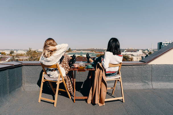 Kaksi viehättävää tyttöä nauttivat teekutsuista katolla näkymät kaupunkiin. Juo terveellistä tattariteetä. Terveydenhuollon tai kasviperäisten lääkkeiden käsite
. - Valokuva, kuva