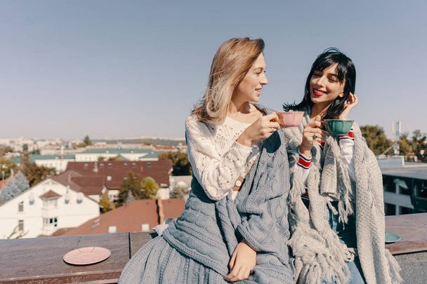 Dwie atrakcyjne dziewczyny cieszą się herbatą na dachu z widokiem na miasto. Picie zdrowej herbaty gryczanej. Koncepcja opieki zdrowotnej lub medycyny ziołowej. - Zdjęcie, obraz