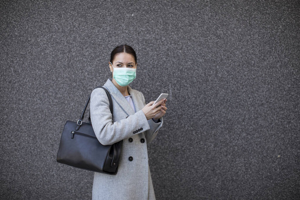 Pretty young woman with protective facial mask on the street using mobile phone - Foto, Bild