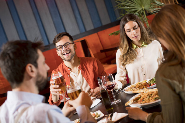 Группа молодых людей ужинает в ресторане - Фото, изображение