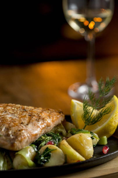 Filetto di salmone con patate gratinate, porro e spinaci in tavola con bicchiere di vino bianco
 - Foto, immagini