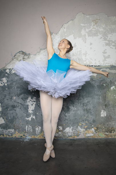 Mooie jonge ballerina danseres dansen klassiek ballet tegen rustieke muur - Foto, afbeelding