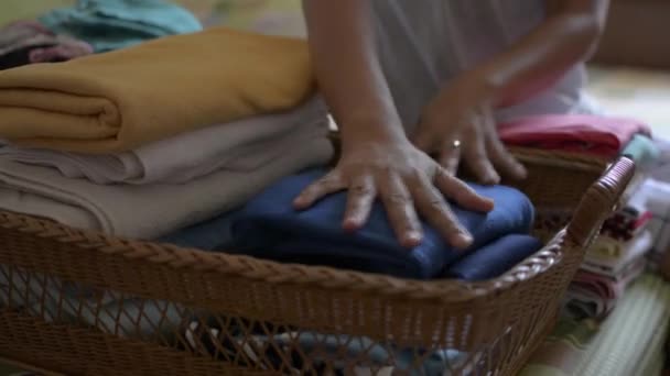 Woman is folding clothes and putting into a wooden basket. Housewife doing some house work in bedroom. Close up a pile of folded clothes on the bed. - Footage, Video