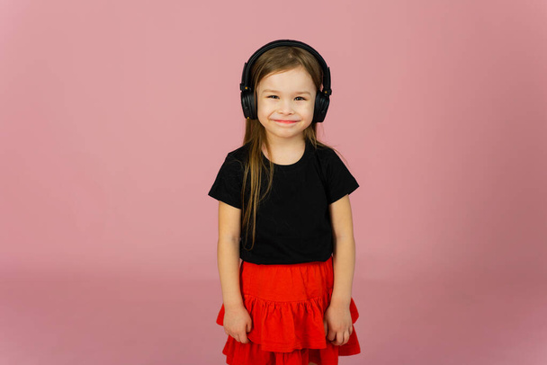Little girl listens to music in big headphones on a pink pastel background. - Photo, Image