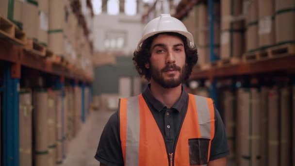 Portret van een serieuze jonge magazijnmedewerker die naar de camera kijkt die tussen de rijen van het magazijn staat - Video