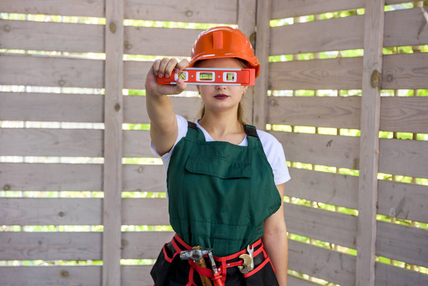 Mujer con herramienta de nivel de medida en el sitio de construcción. Mujer midiendo pared de madera y posando para cámara
 - Foto, Imagen