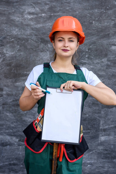 Mujer con uniforme protector y casco posando con portapapeles y cinturón de herramientas
 - Foto, Imagen