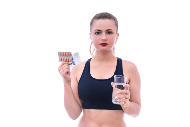 Woman in sportswear holding pill and glass of water isolated on white - Photo, Image