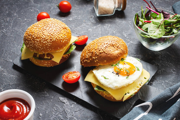 Aamiainen kaksi hampurilaista kanalla, paistettua munaa ja juustoa tummalla kivipohjalla
 - Valokuva, kuva
