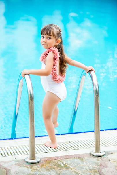 Young beautiful little girl in a bathing suit making water splash at the swimming pool.Enjoying summer and having fun. Vacation mood - Fotó, kép