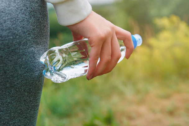 A bottle of clean drinking water in a woman's hand. Concept of drinking water for health. - Zdjęcie, obraz