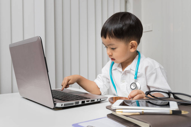 Little boy in medic uniform using a laptop on desk - Foto, immagini